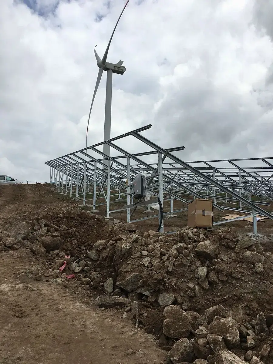 GES konstrüksiyon montajı — arazi üzeri çelik taşıyıcı yapı ve rüzgar türbini